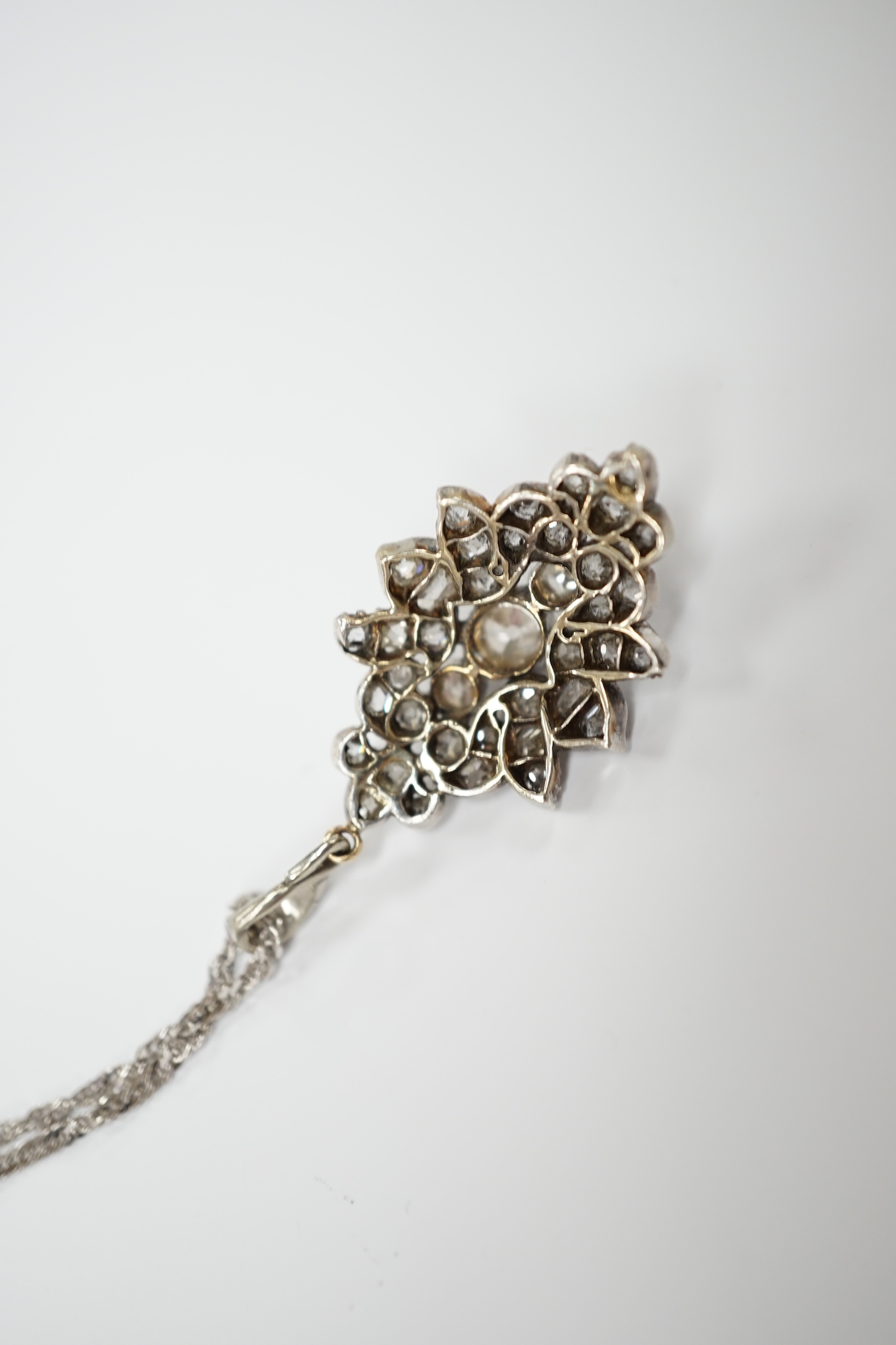 A white metal and diamond cluster set oval pendant, 27mm, on 9kt white metal chain, gross weight 5.8 grams.
